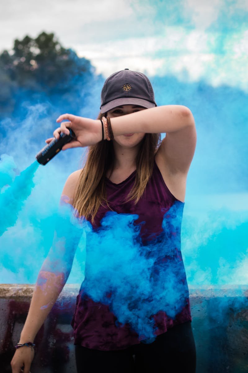A stylish woman surrounded by bright blue smoke outdoors, creating a dynamic fashion statement.